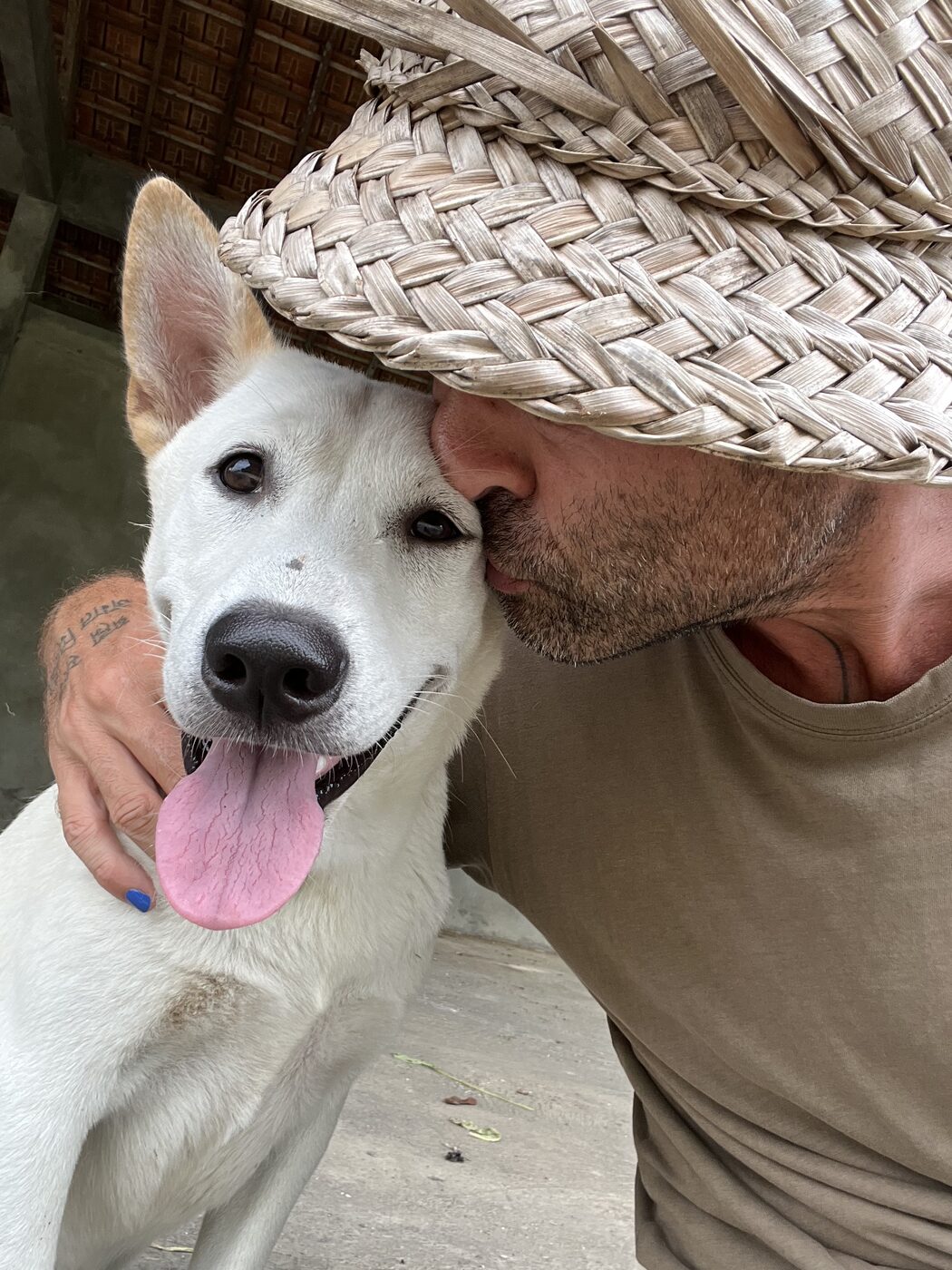 Stephan Mairesse in a straw hat nuzzling a white dog